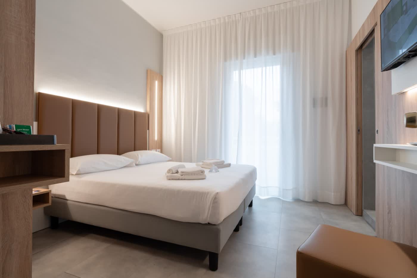 Camera dell'Hotel Iris a Jesolo con testiera in legno e tende chiare